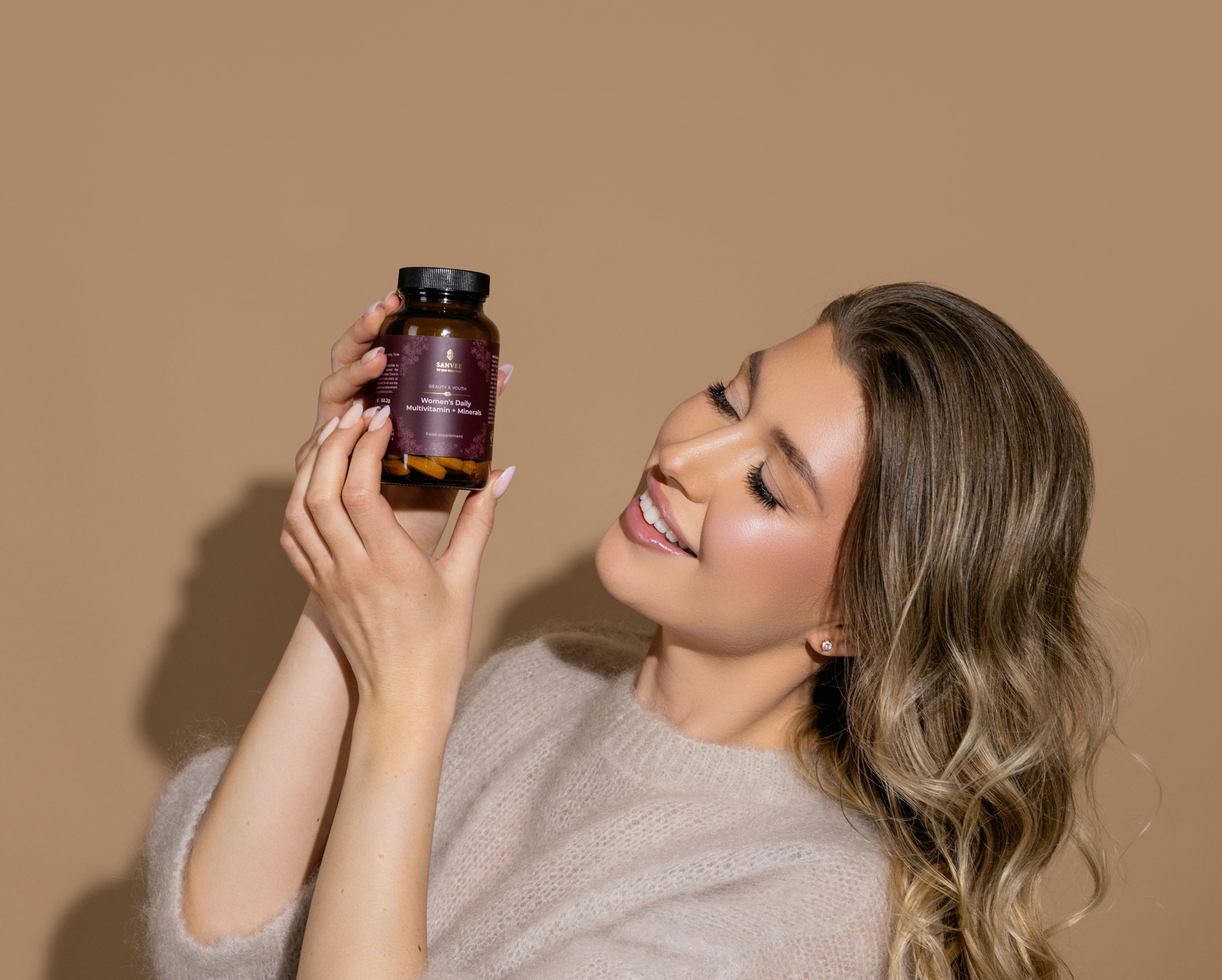 Woman holding Sanvee women's daily multivitamin bottle and smiling in profile