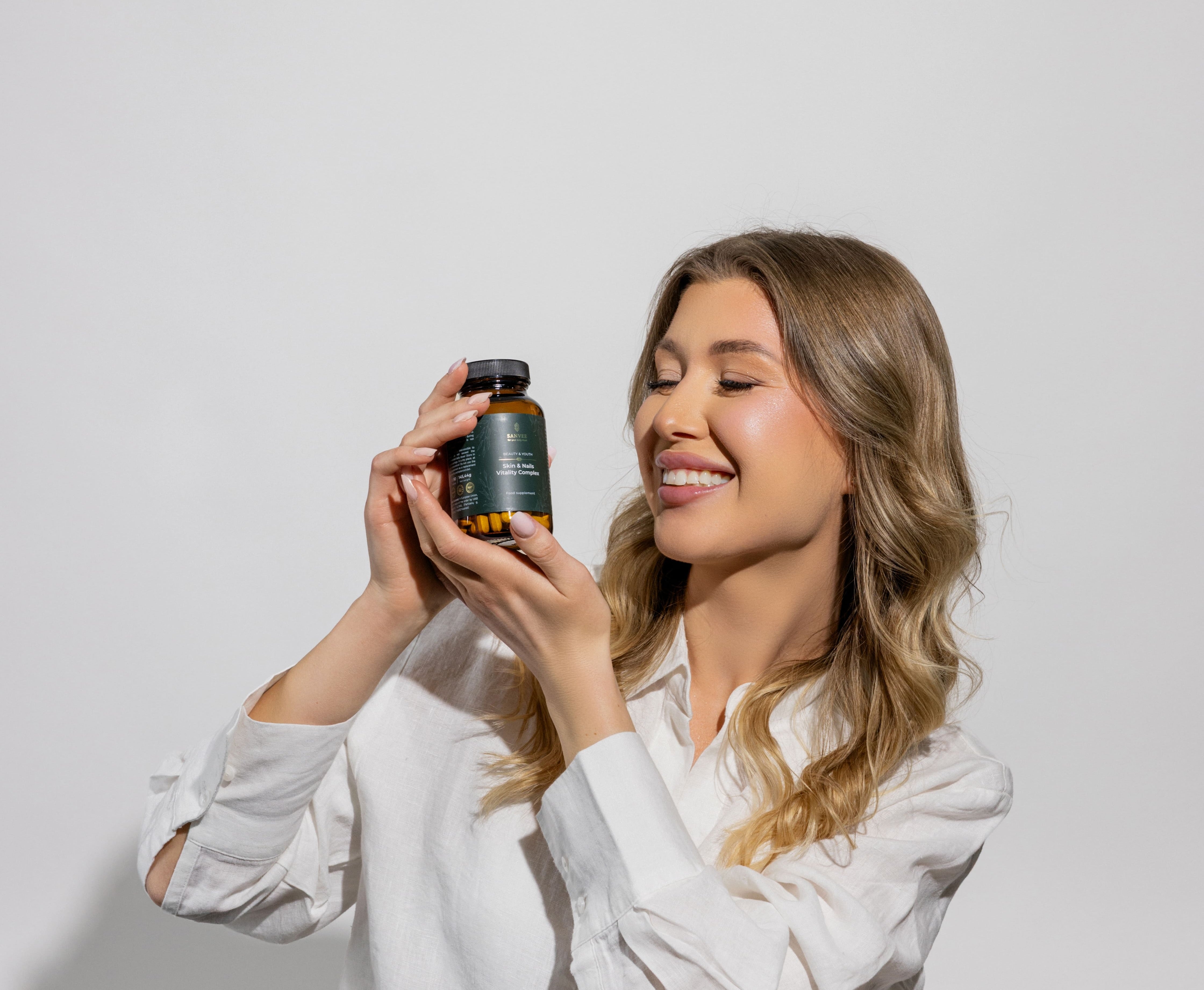 Woman holding Sanvee skin and nails supplement bottle with vitality complex capsules