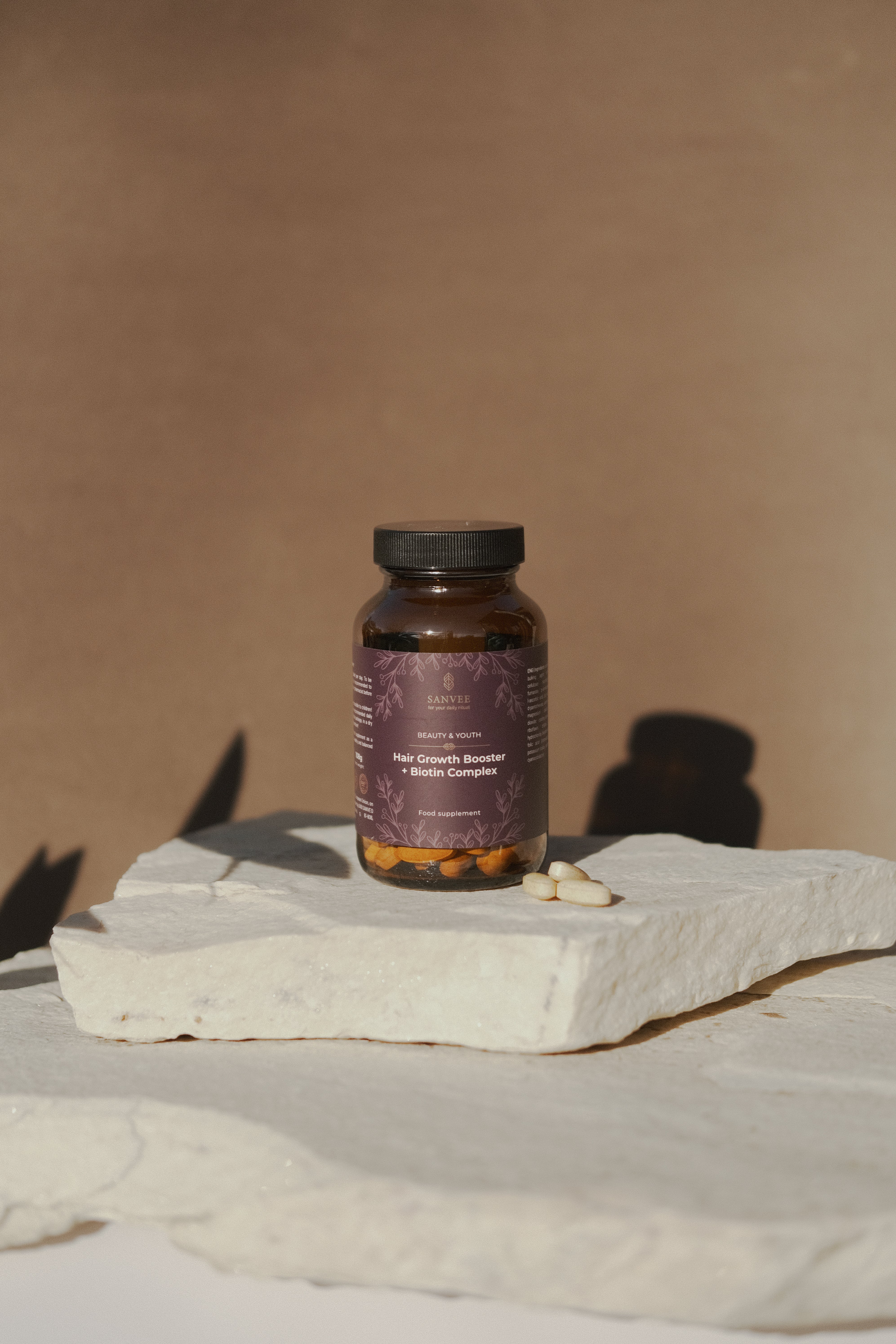 Hair growth supplement with biotin complex by Sanvee in glass bottle with capsules on stone surface